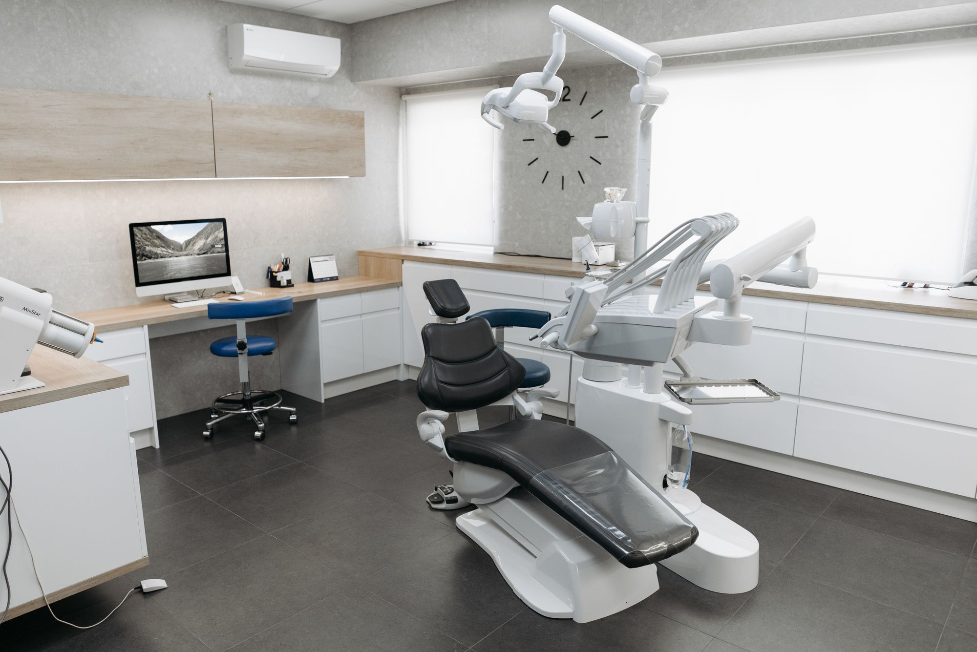 Black dental chair and examination equipment in a bright clinic with white cabinets and wood counters.