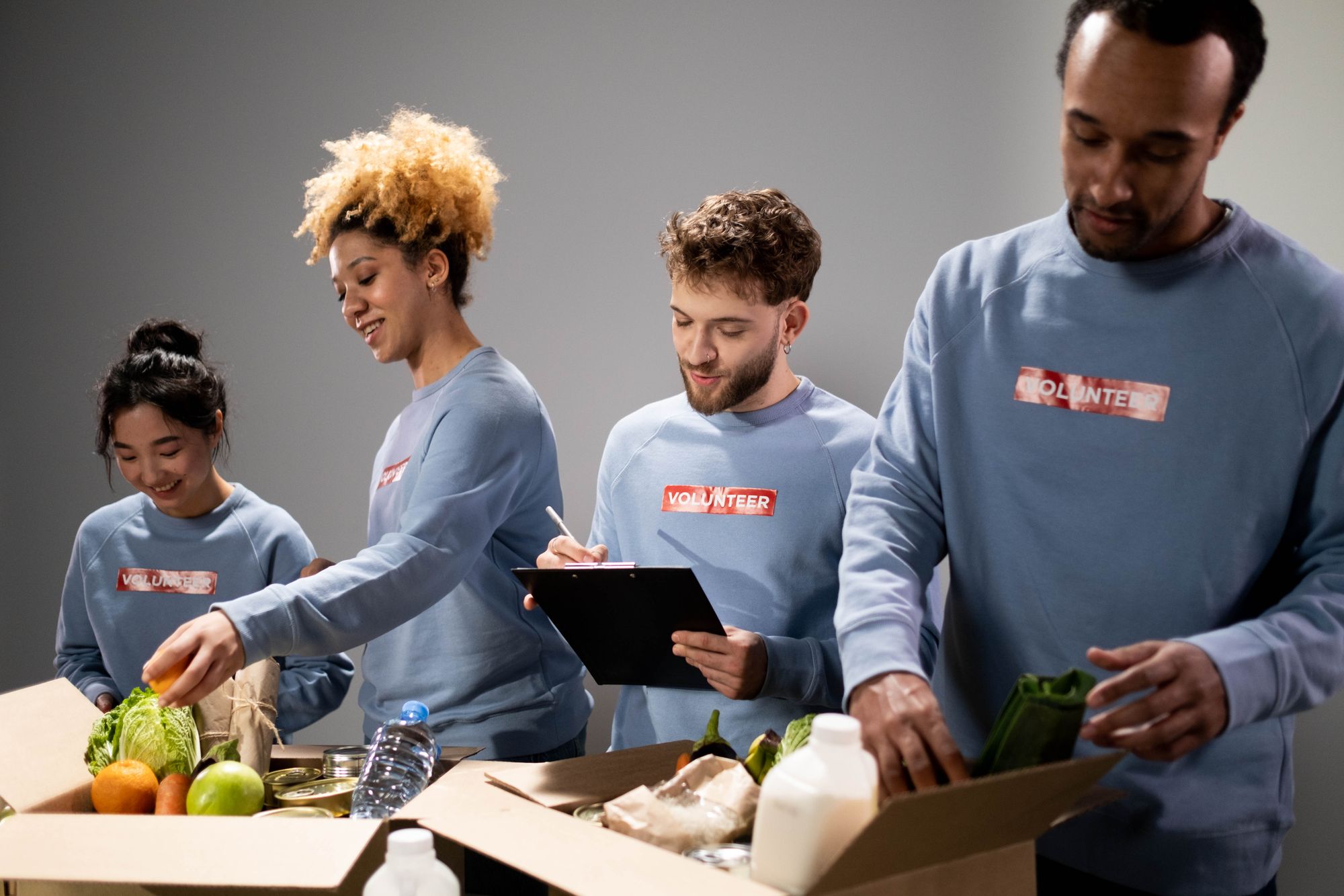 Four volunteers pack fresh produce and canned food into cardboard donation boxes.